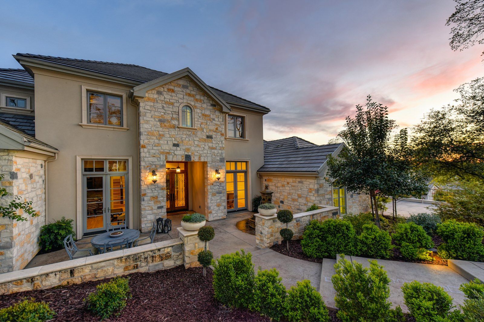 Stone home exterior with landscaped walkway and patio at dusk